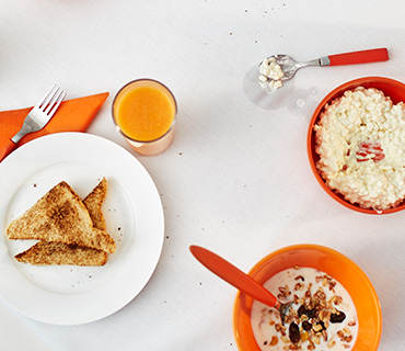 An image of a breakfast table with toasts, oatmeal, muesli, and orange juice