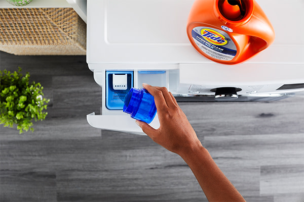 A person pouring Tide liquid detergent into the detergent drawer 
