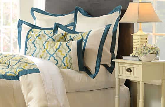 A bedroom set displaying a blue, yellow and cream bedspread and a small bedside table with lamp