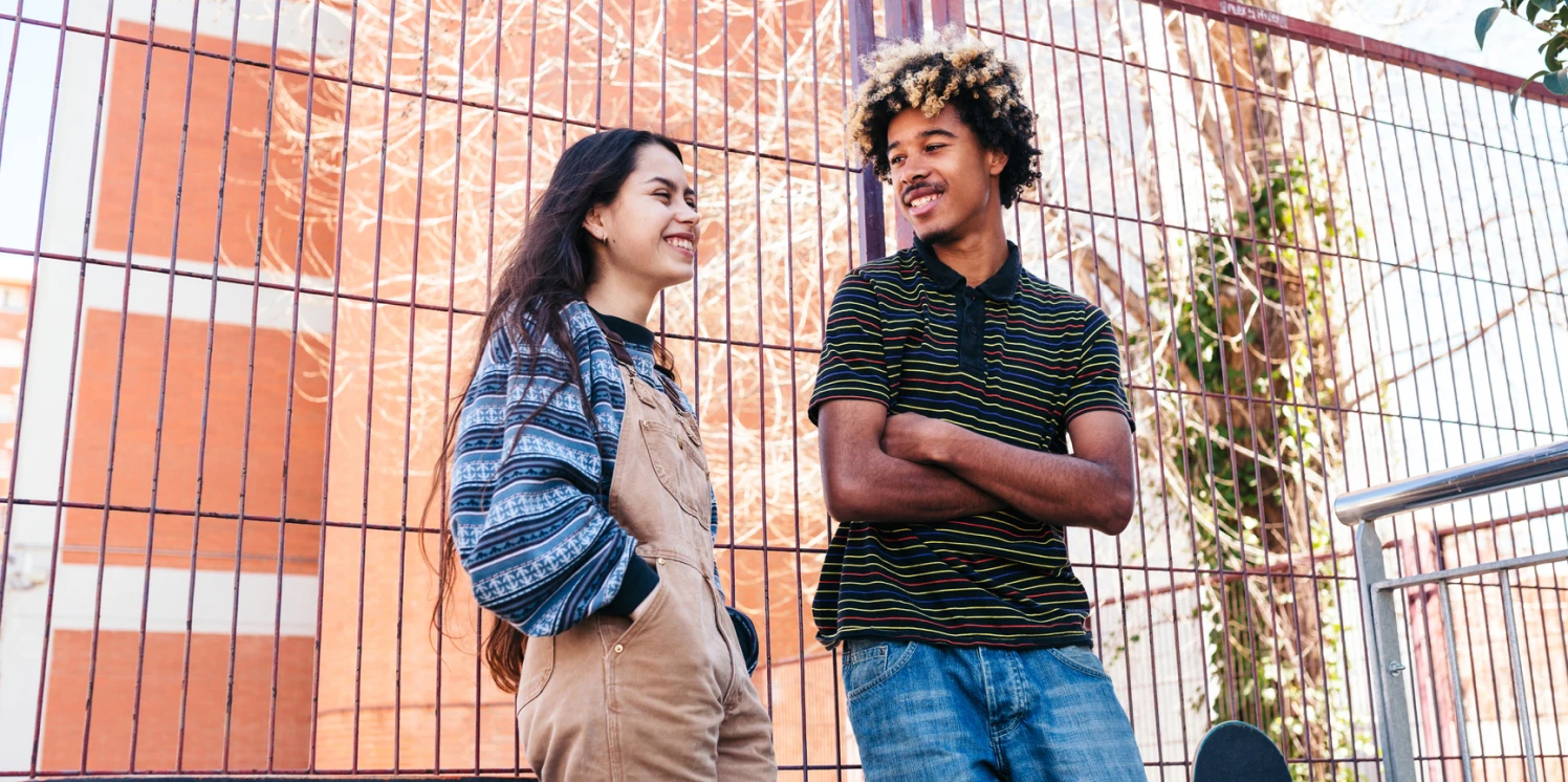 Een jong stel van rond de 20 staat bij een hek van een bouwproject.