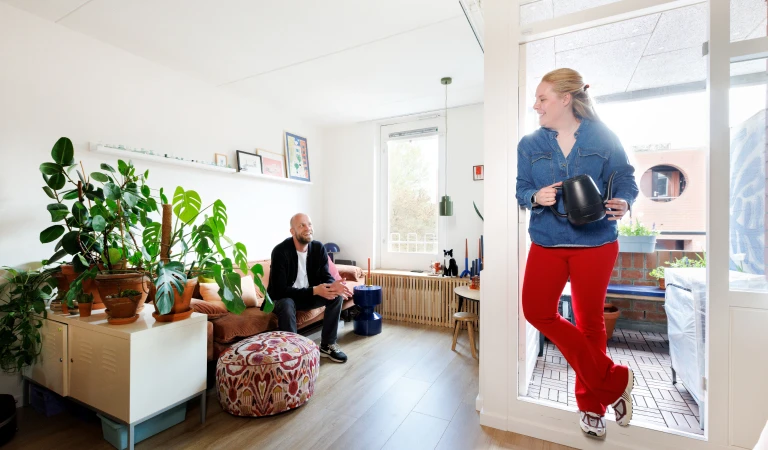 Hannah staat in de deuropening van haar balkon met zicht op de huiskamer.