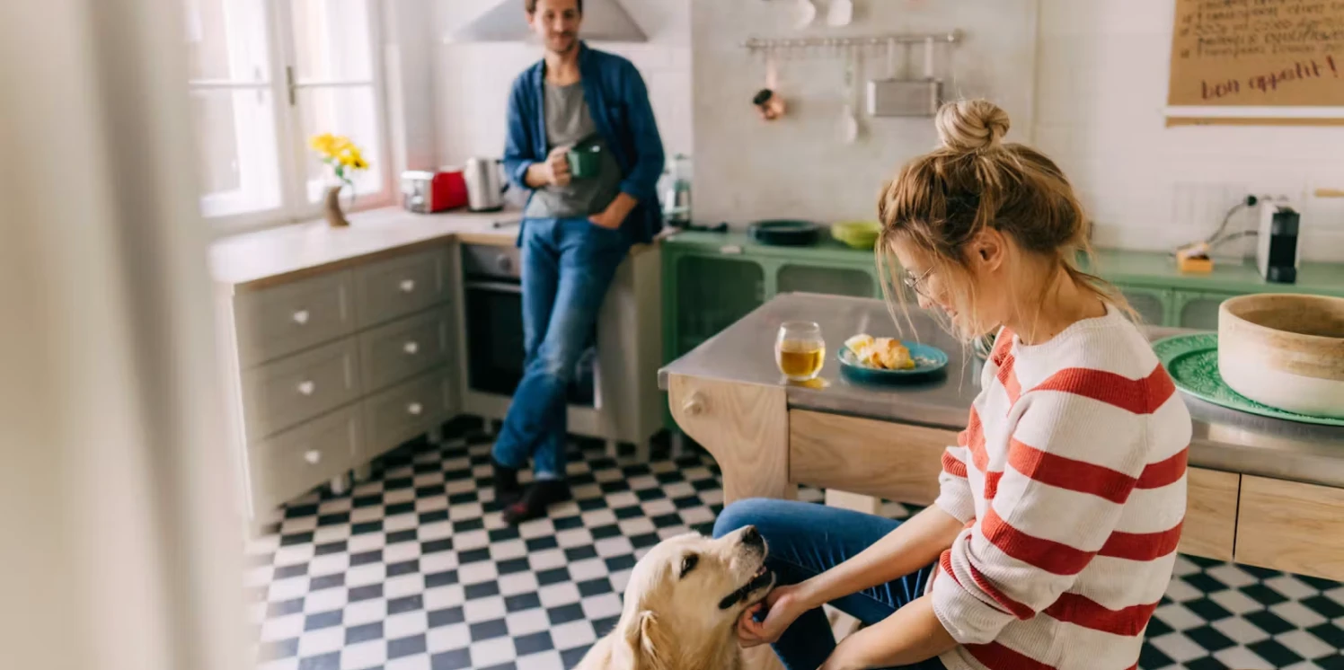 Een man en vrouw staan in de woonkeuken met zwart-wit geblokte vloer, terwijl de vrouw hun labrador aait.