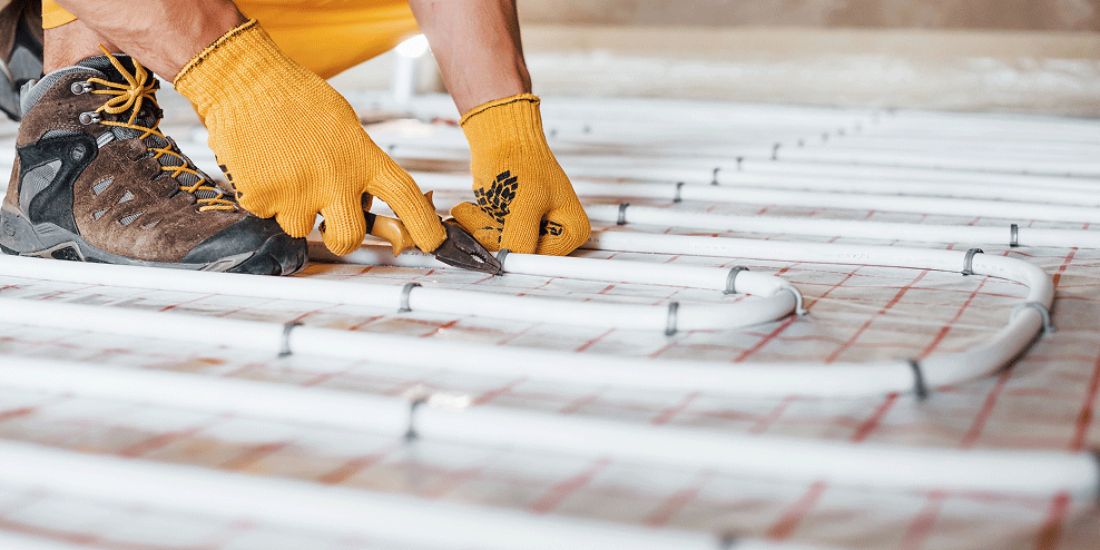 Ingezoomd beeld van hand die buizen voor vloerverwarming monteert aan een ondervloer. 