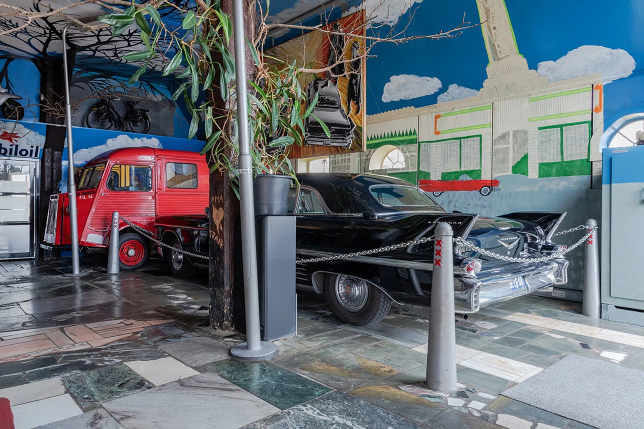 Binnen in de woonboerderij staat een zwarte Cadillac achter de plant geparkeerd, met op de achtergrond een rode truck.