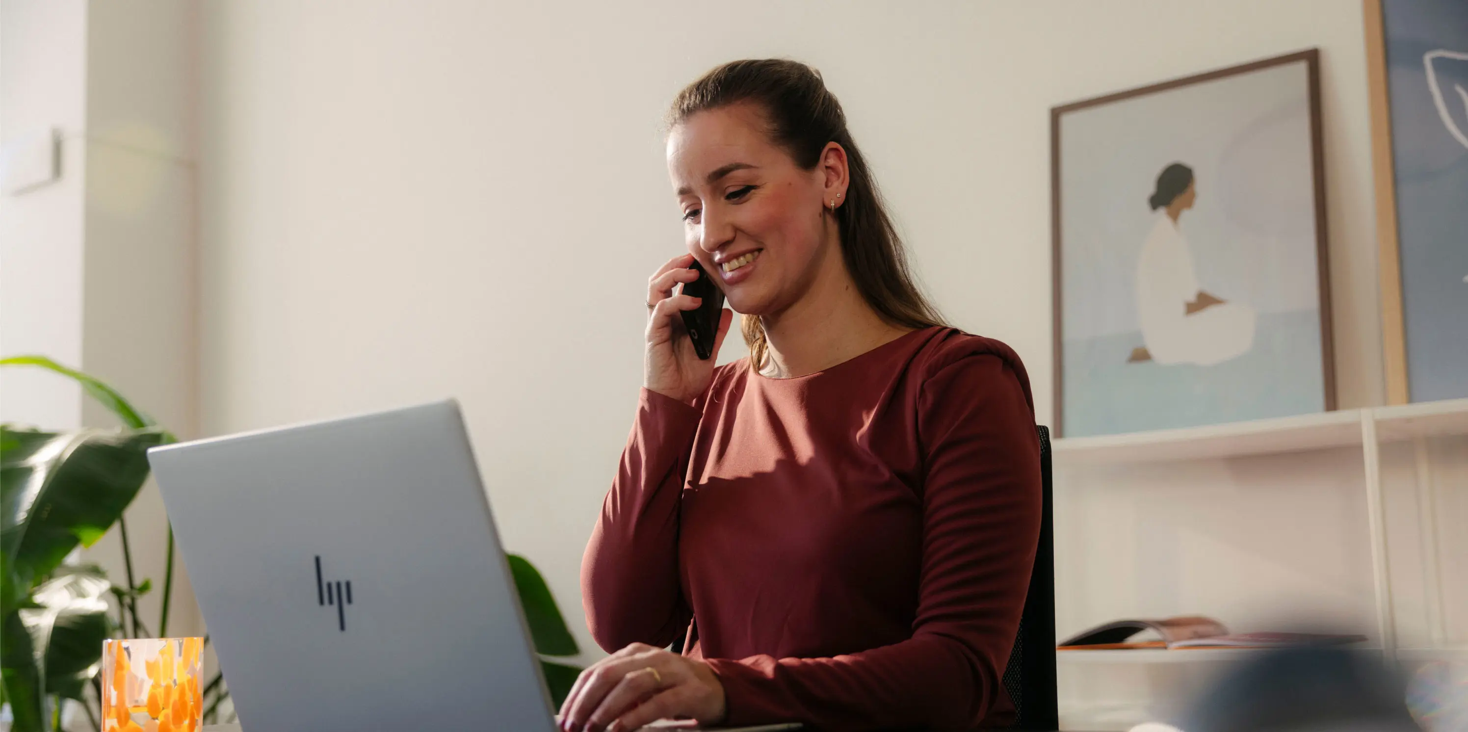 Bellende vrouw met telefoon in haar hand zit achter laptop.