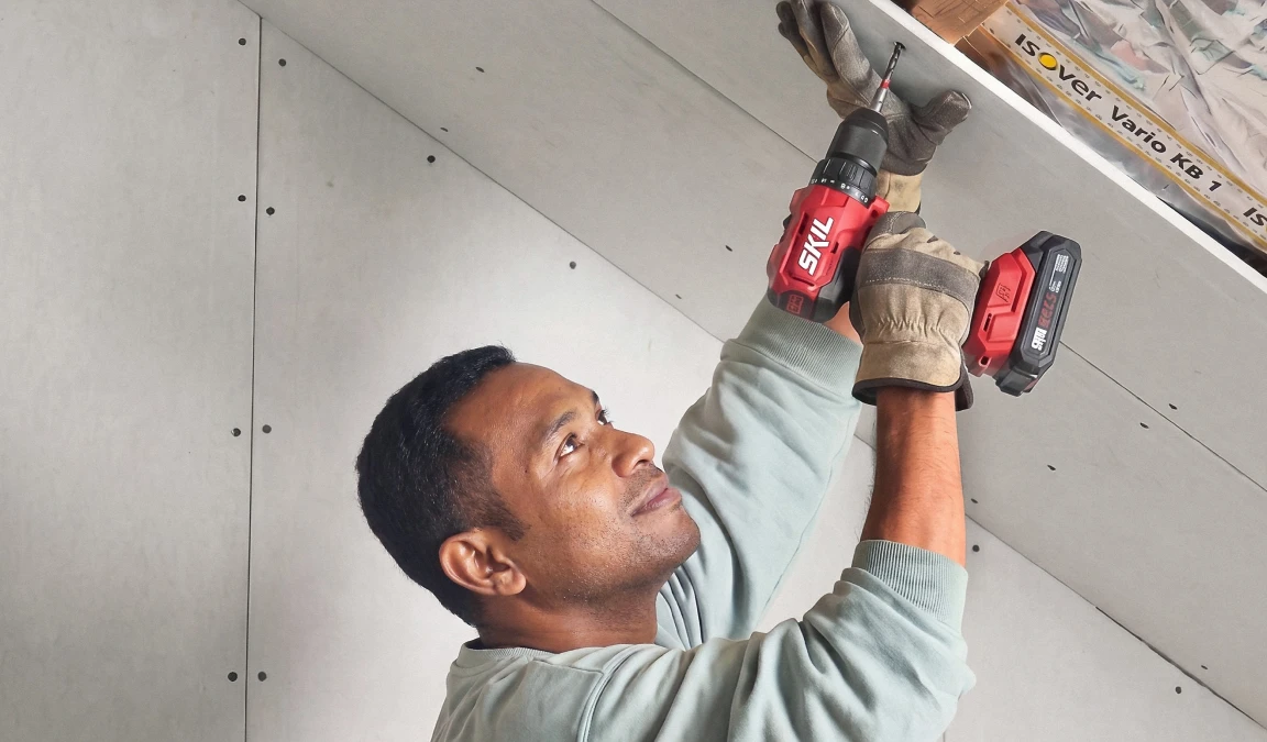Man met schroefmachine is bezig om een plafond te isoleren.
