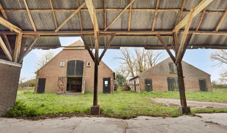 Doorkijkje naar de achterzijde van het woonhuis en de naastgelegen schuur van wederopbouwboerderij 't Heyendaal. Genomen vanonder een afdak.