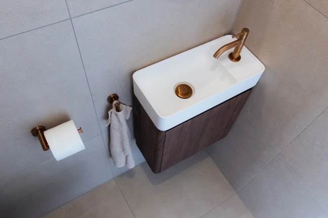 Klein toiletmeubel van bruin hout met ingebouwde, witte wastafel en messing kraan.
