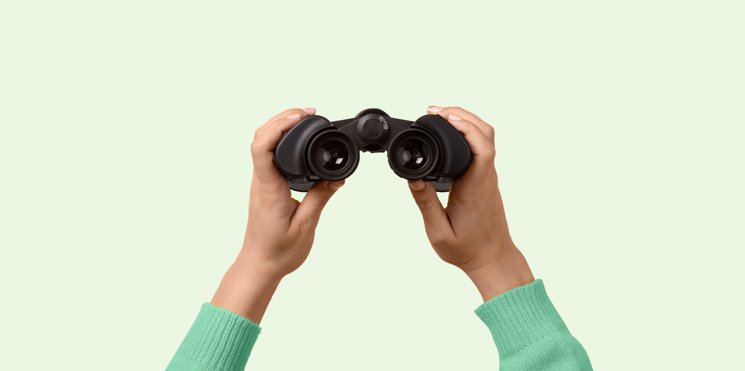 Twee handen houden een verrekijker vast, metafoor voor 'verder kijken dan kliks'.