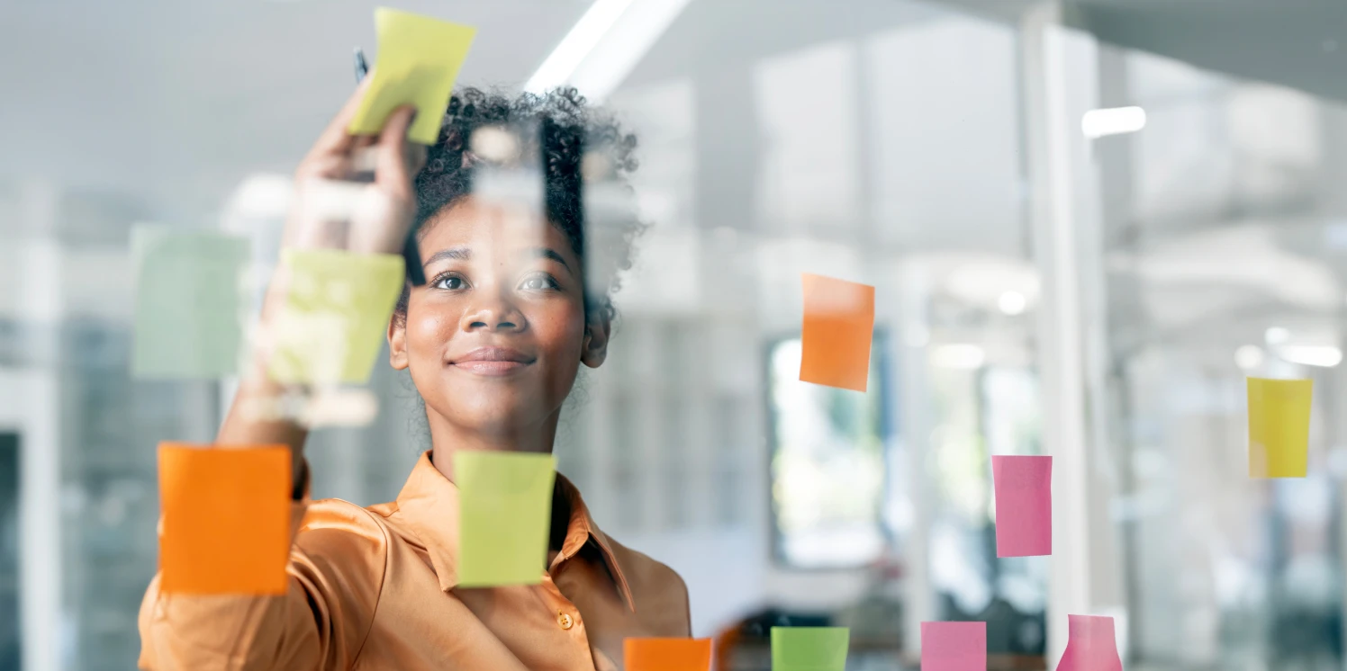 Jonge zwarte vrouw plakt post-its op een glazen wand.