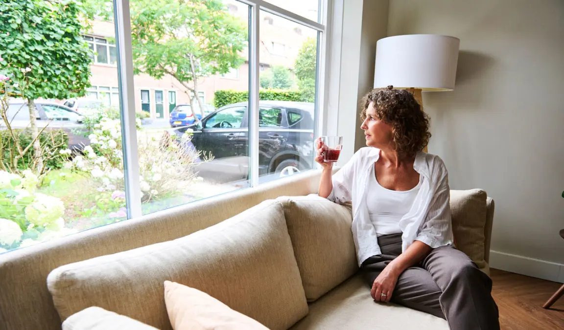 Nanda zit op de beige bank met een kop koffie voor het raam van haar woning in Zeist.