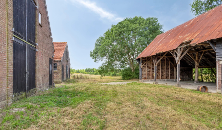 Blik op het erg van wederopbouwboerderij 't Heyendaal, met links het woonhuis en de schuur en rechts de overdekte stalling voor landbouwvoertuigen.