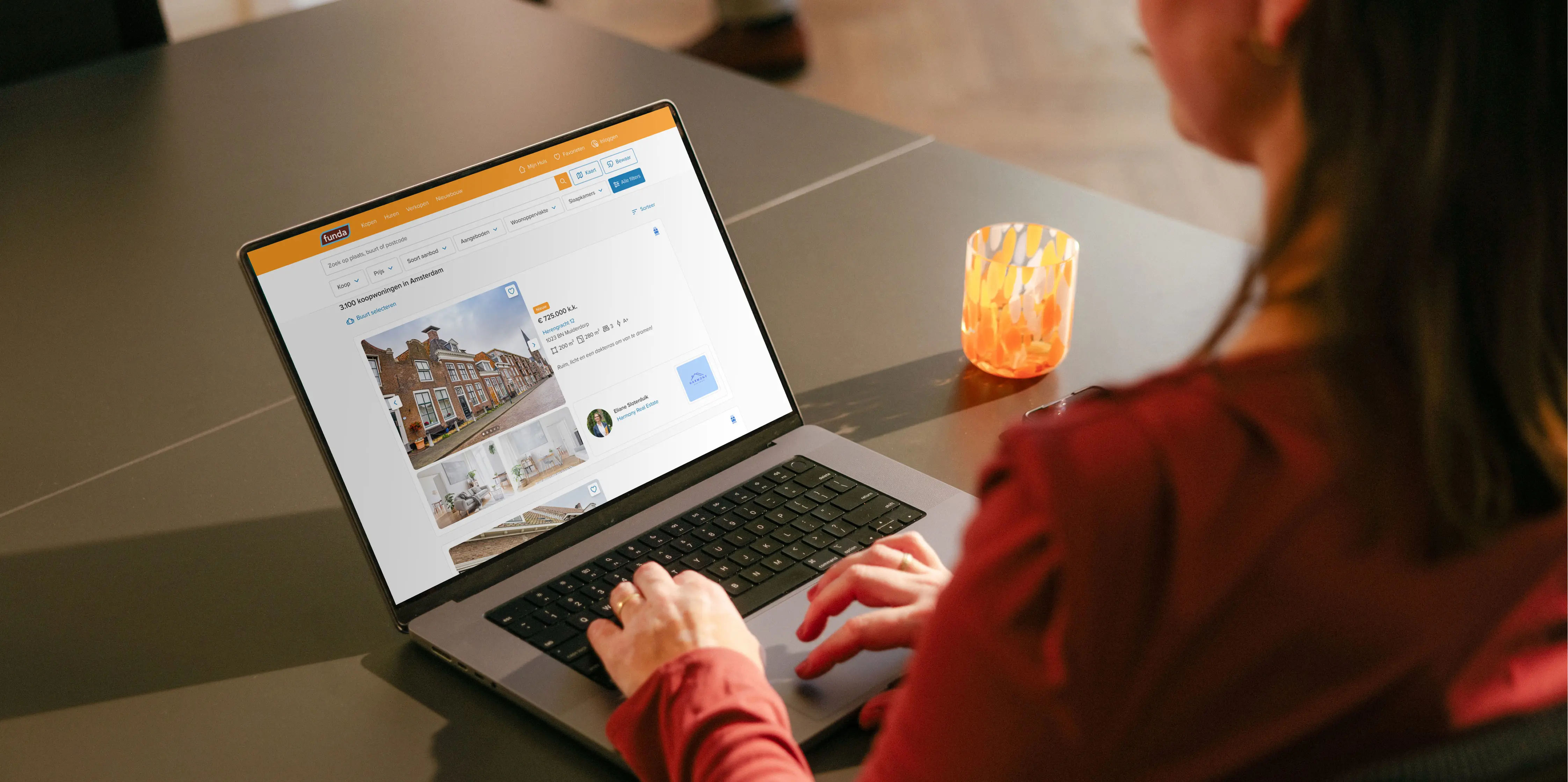 Een vrouw met lang donker haar en rode blouse zit achter haar laptop naar huizen op Funda te kijken.