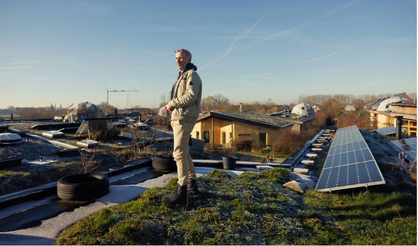 Paul staat op het groene mosdak van zijn aardehuis met achter hem zonnepanelen.