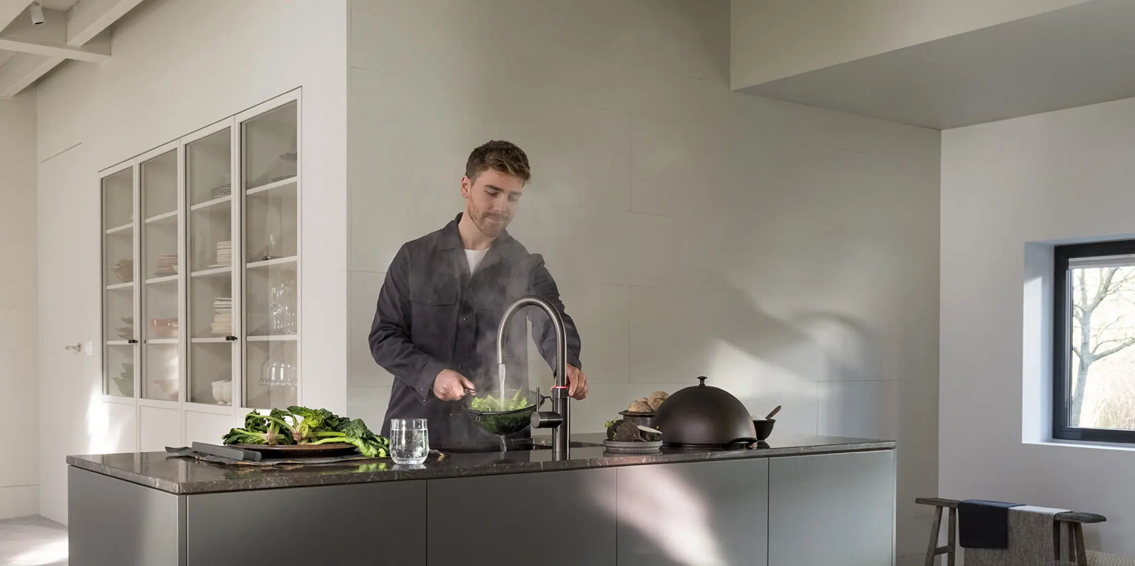 Een man staat achter een kookeiland met een Quooker-kraan en tapt heet water.