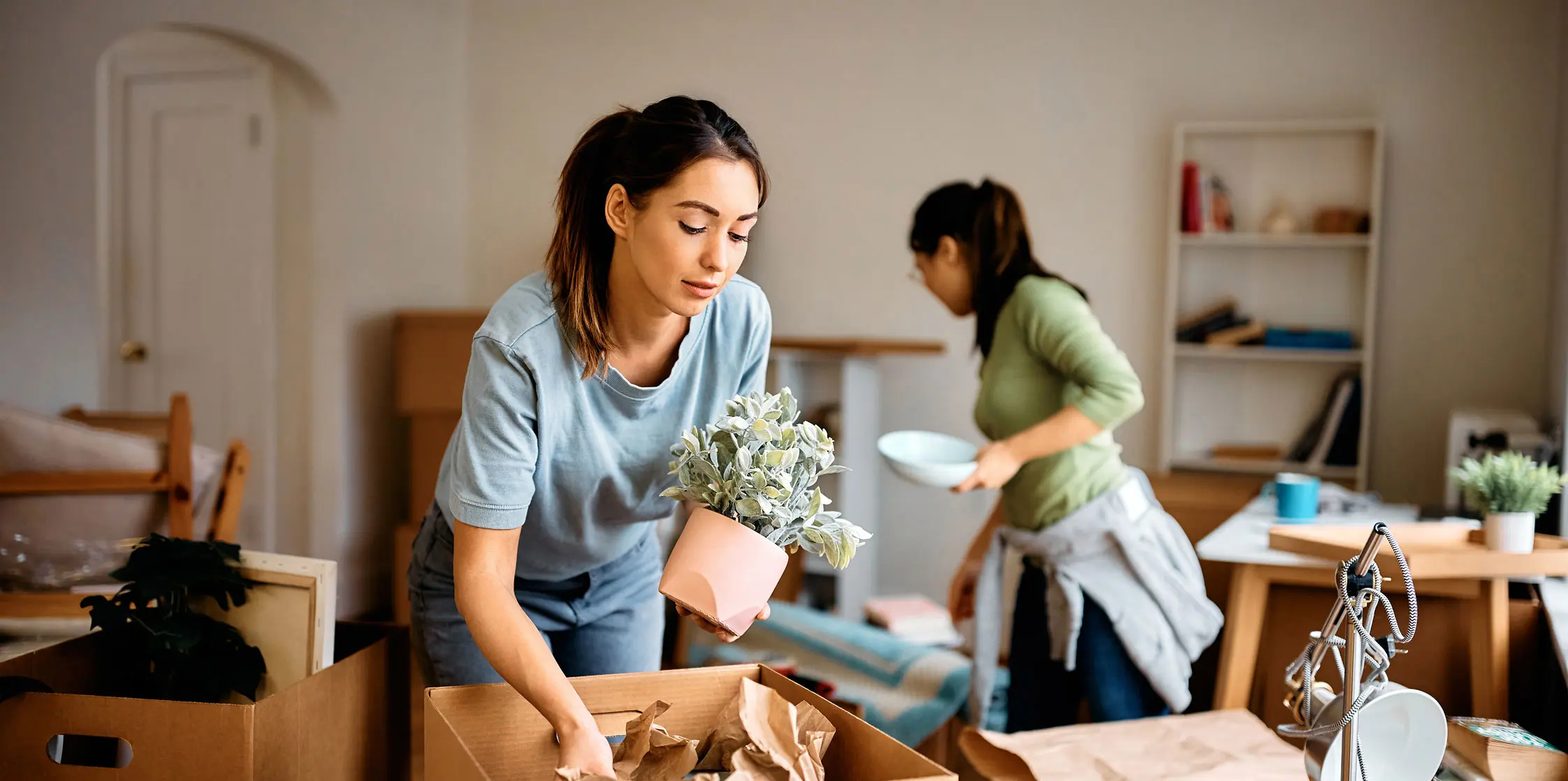 Twee jonge vrouwen zijn dozen aan het uitpakken na een verhuizing naar een nieuw huis.