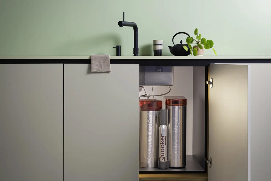 Een openstaand mintgroen gootsteenkastje met daarin een Quooker-reservoir voor warm of kokend water en een Quooker CUBE voor gekoeld en bruisend water.