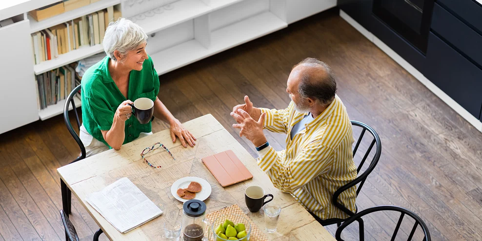 Een 55-plus-koppel zit te overleggen aan een eettafel.