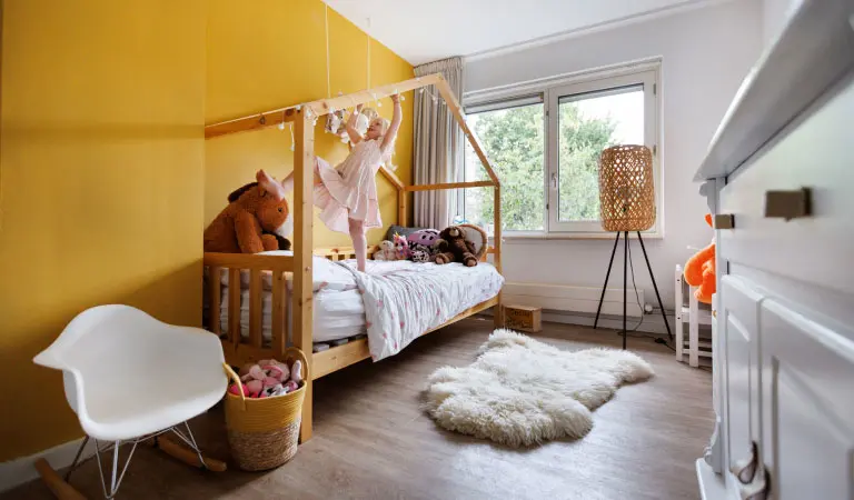 Dochter hangt aan houten frame boven haar bed in haar kamer met links een gele muur.