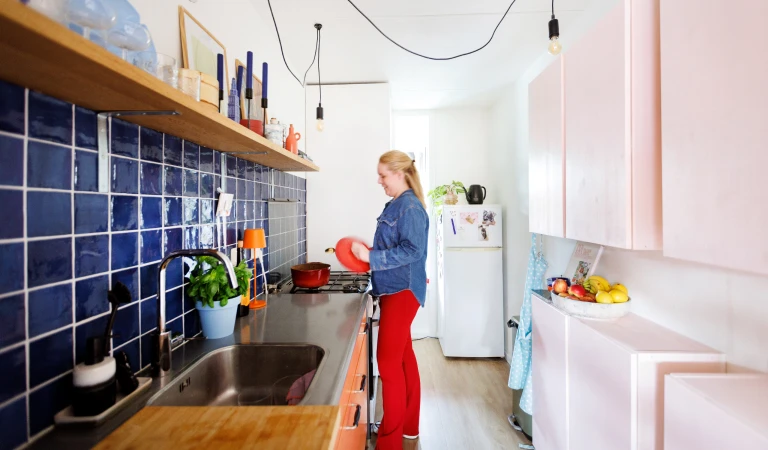 Hannah in de opgeknapte keuken met donkerblauwe tegels en lichtroze en oranje keukenkastjes.