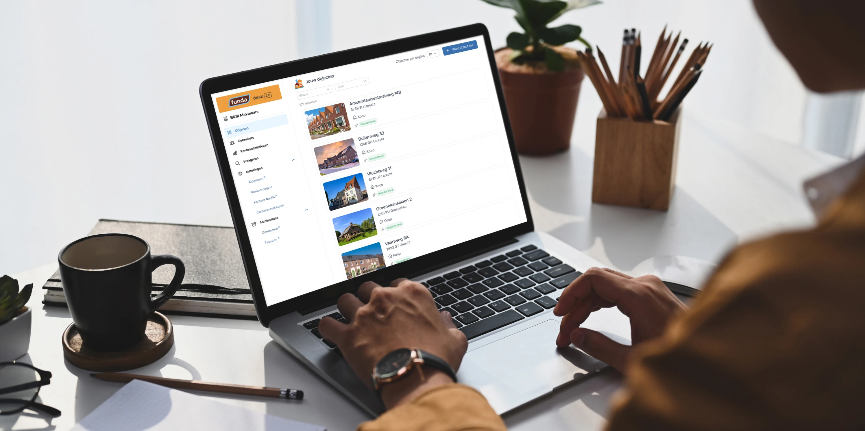 Een medewerker van een makelaarskantoor achter een laptop met objecten van Funda op het scherm.