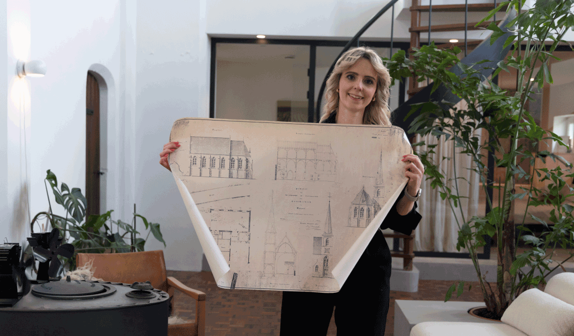 Katy laat in haar handen een bouwtekening zien met daarop de plattegrond en dwarsdoorsnede van de kerk. 