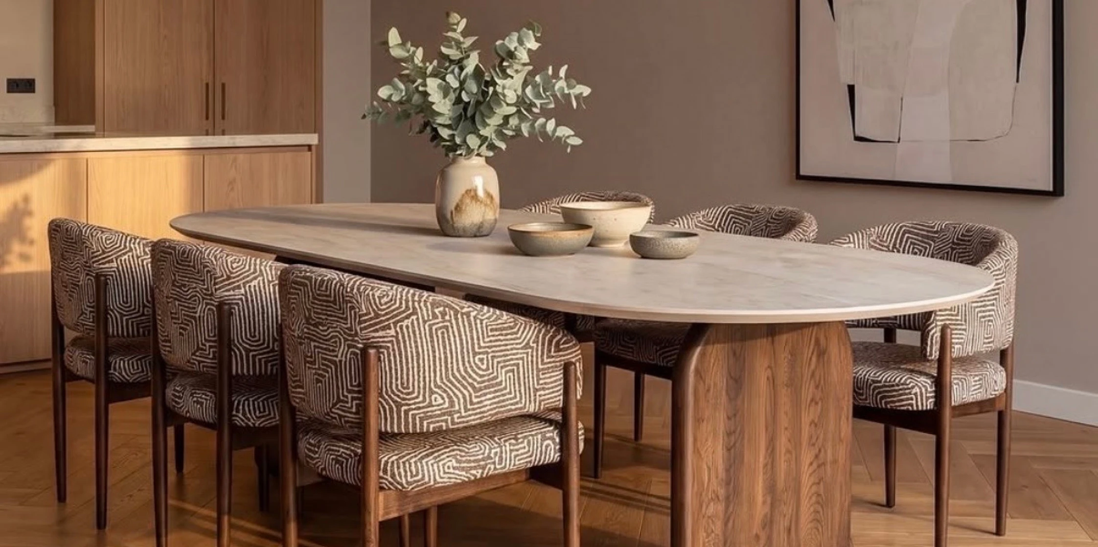Sfeerbeeld van ovalen eettafel met licht tafelblad en houten onderpoot. Eromheen zes ronde stoelen in bruin-wit.