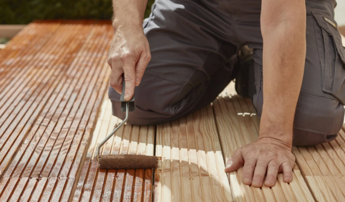 Man is bezig met het beitsen van houten vlonderplanken.