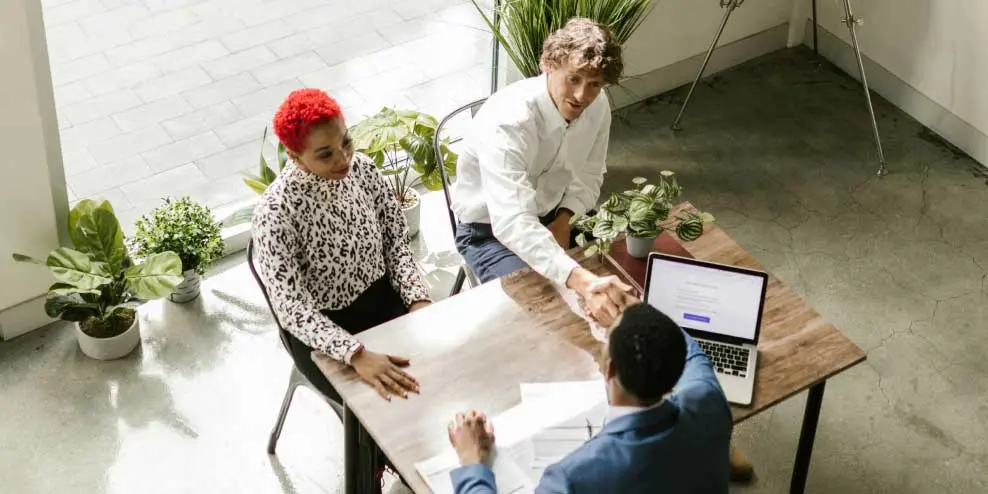 Man van stel schudt hand van makelaar op kantoor ter bevestiging van de makelaarscourtage die zij overeen zijn gekomen.