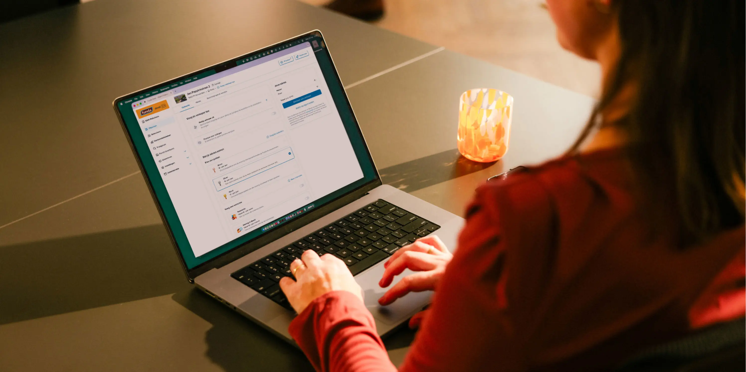 Vrouw achter laptop, waarop de pagina van Funda te zien is waarop een presentatiepakket kan worden gekozen,