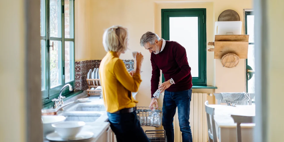 55-plus vrouw en man staan in de keuken bij de afwasmachine.