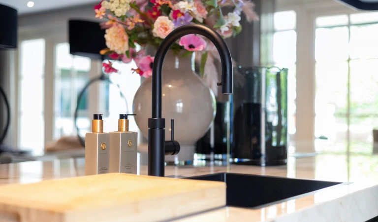 Zwarte kraan en zwarte wasbak in wit marmerkleurig aanrechtblad