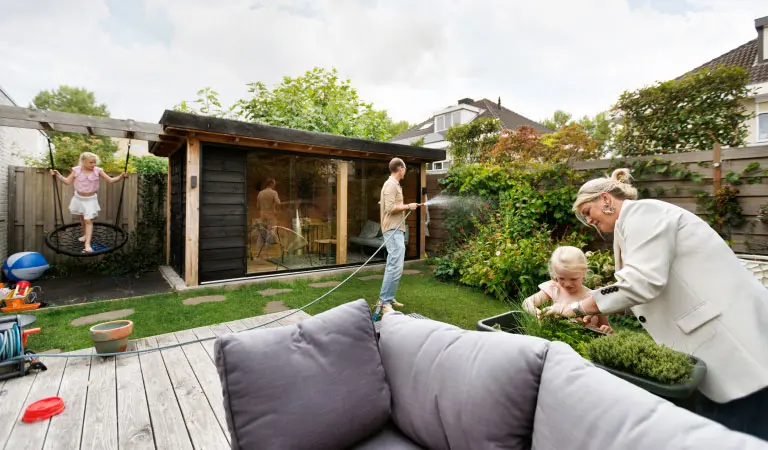 Maarten sproeit de planten in zijn achtertuin, terwijl zijn vrouw en dochter plantjes planten in een bak.