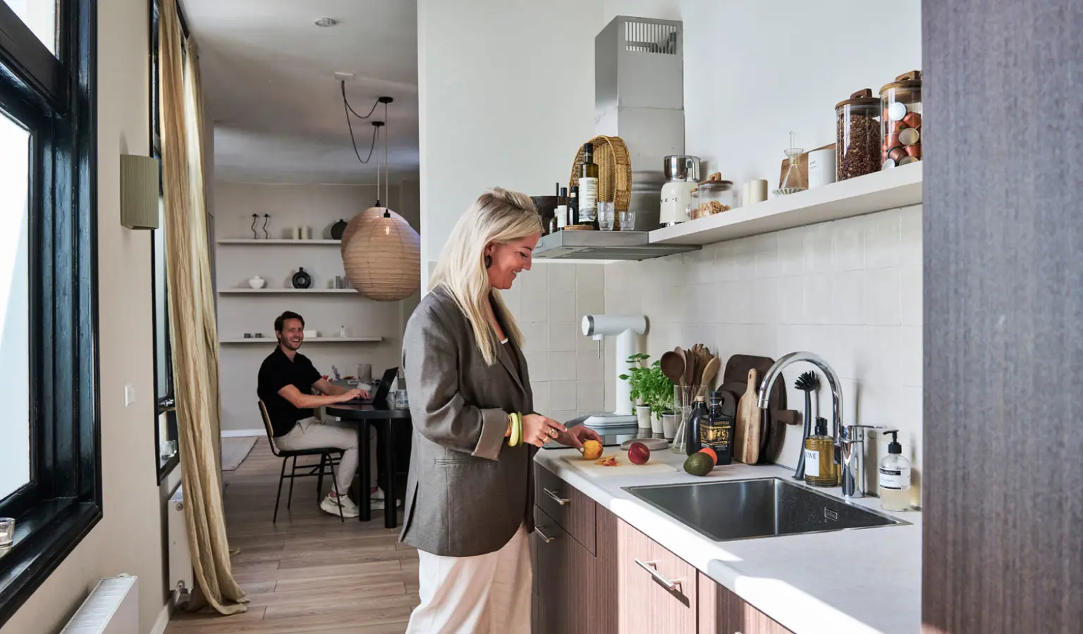 Sascha staat aan het aanrecht en Martijn zit op de achtergrond aan de keukentafel in hun bovenwoning in Leiden.