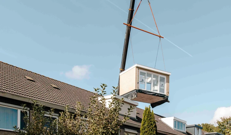 Prefab dakkapel wordt met hijskraan op dak gehesen.