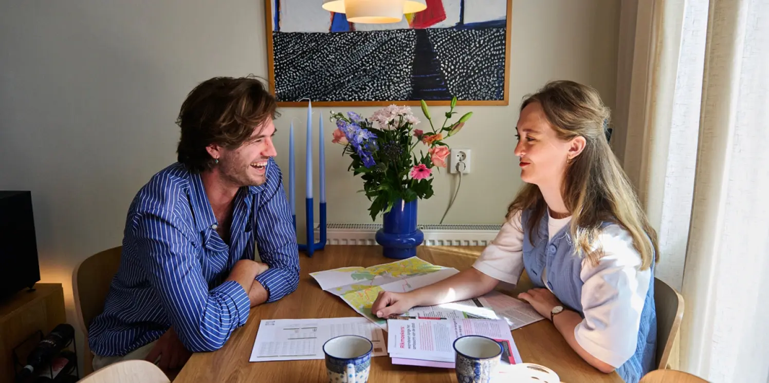 Starters Joost en Myhrte zitten aan de houten eettafel met papieren voor hun neus.