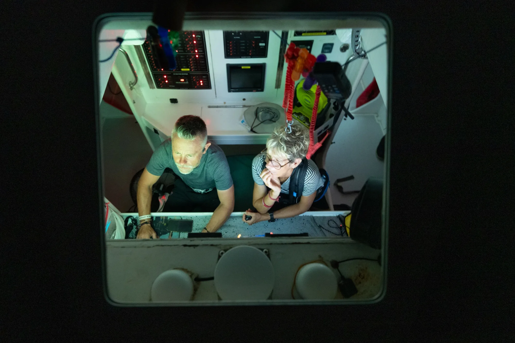 Overhead view of two Clipper Race crew members working at the yacht’s navigation station, monitoring instruments and navigation systems during an offshore ocean race.