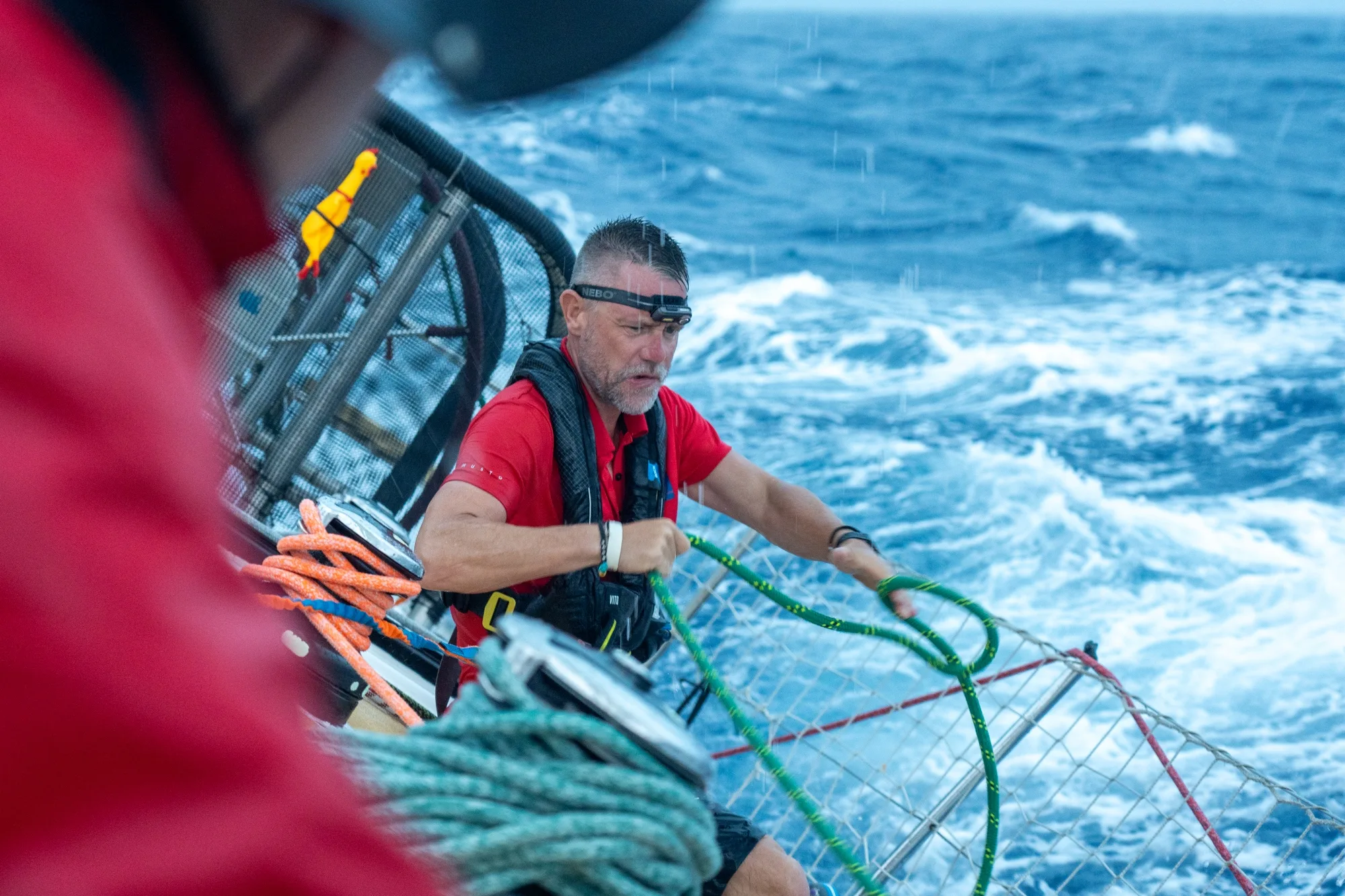 London Business School (LBS) Skipper Gavin Reid working on deck during an offshore ocean race, handling sailing lines as the yacht powers through rough sea conditions.