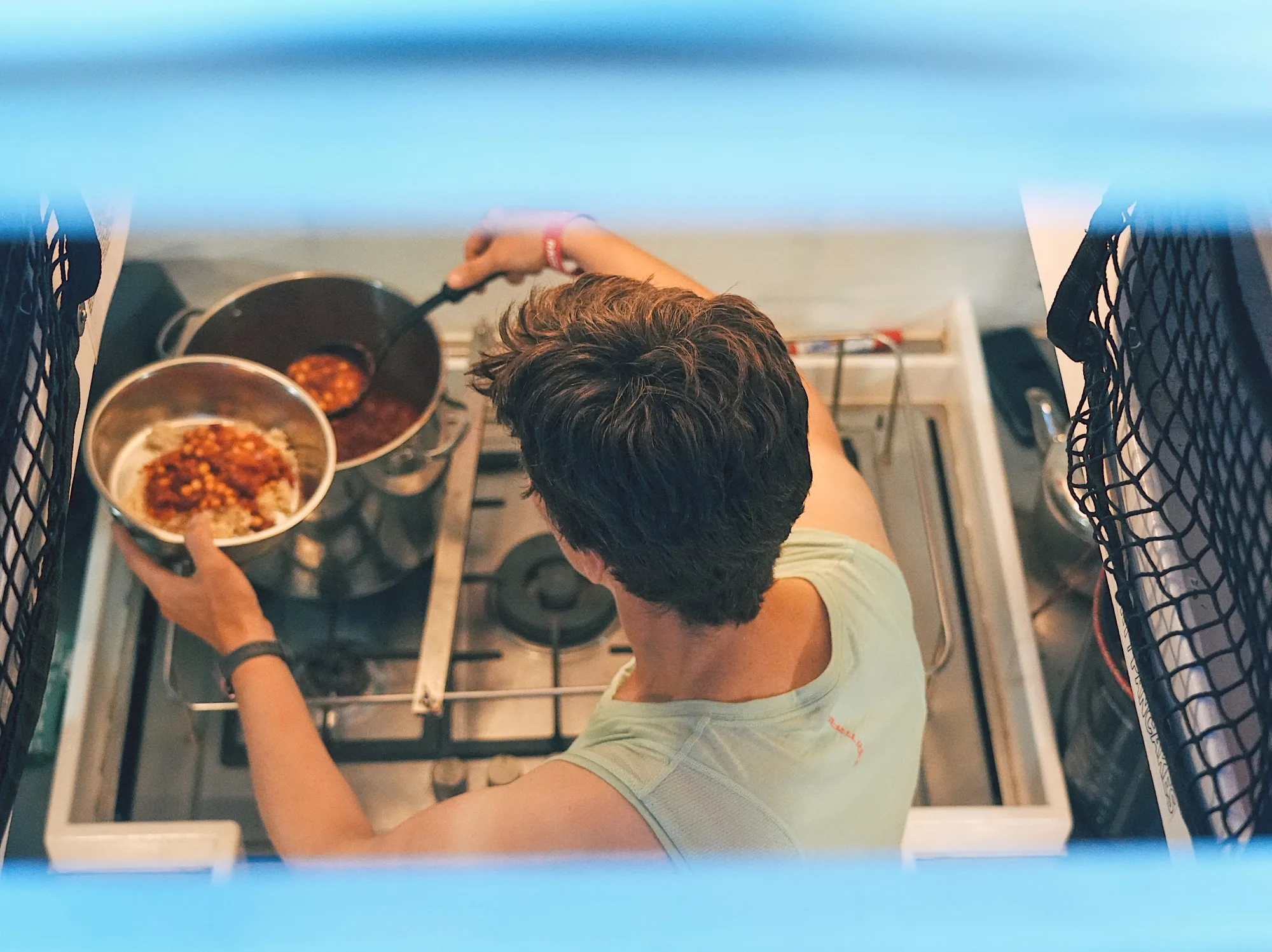 Overhead view of a Clipper Race crew member cooking a meal in the yacht’s galley, preparing food on a stove during an offshore sailing race.