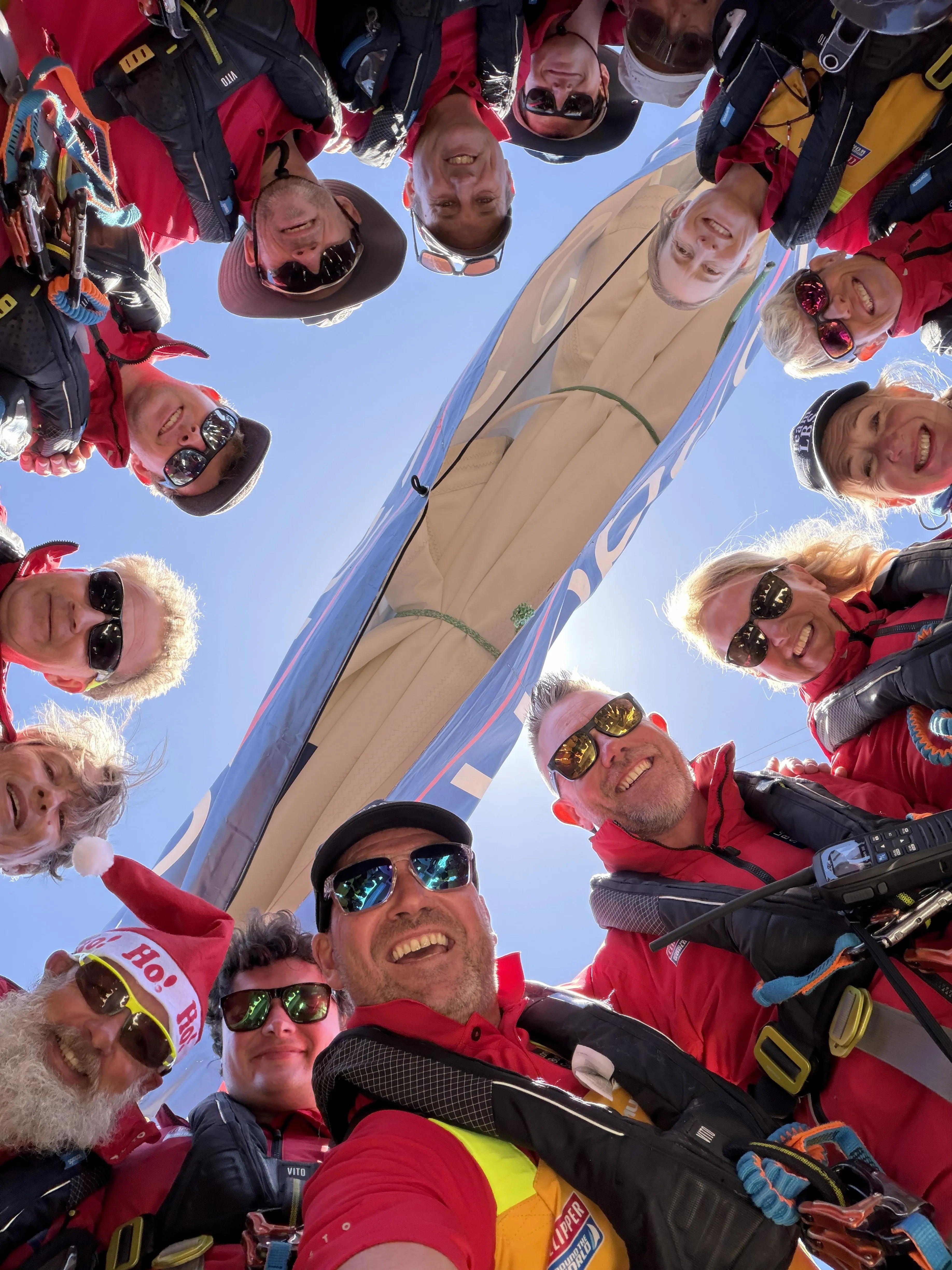 Team London Business School crew members gathered in a circle on deck, smiling for a group selfie aboard their Clipper Race yacht during an offshore sailing challenge.