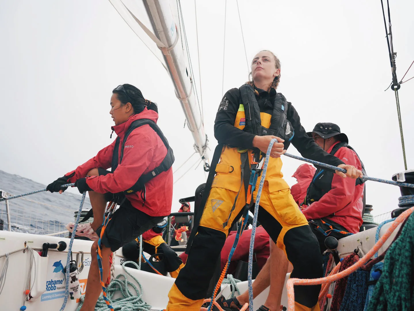 Crew members aboard a racing yacht manage sails and rigging at sea, showcasing teamwork, skill, and endurance in offshore yacht racing conditions.