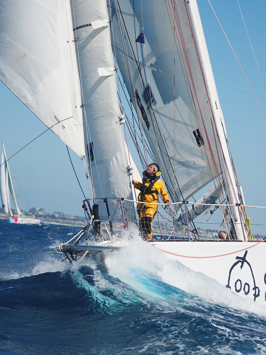 Crew member aboard the Great Ormond Street Hospital (GOSH) Clipper Race yacht standing at the bow as the yacht sails through waves under full sail during an offshore ocean race.