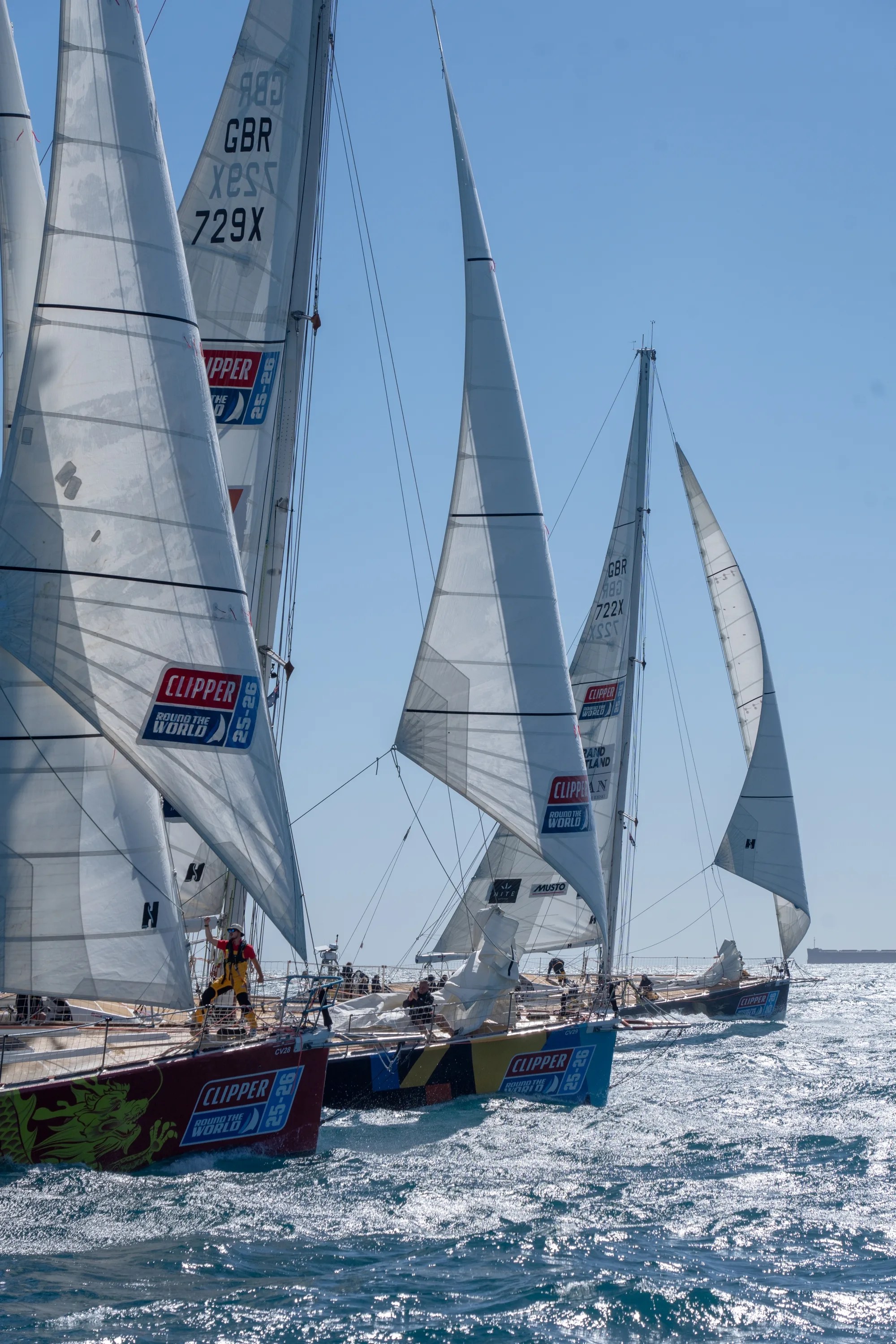 Several Clipper Race yachts sailing in close formation during an offshore race, with crews competing for position on open water under full sail.