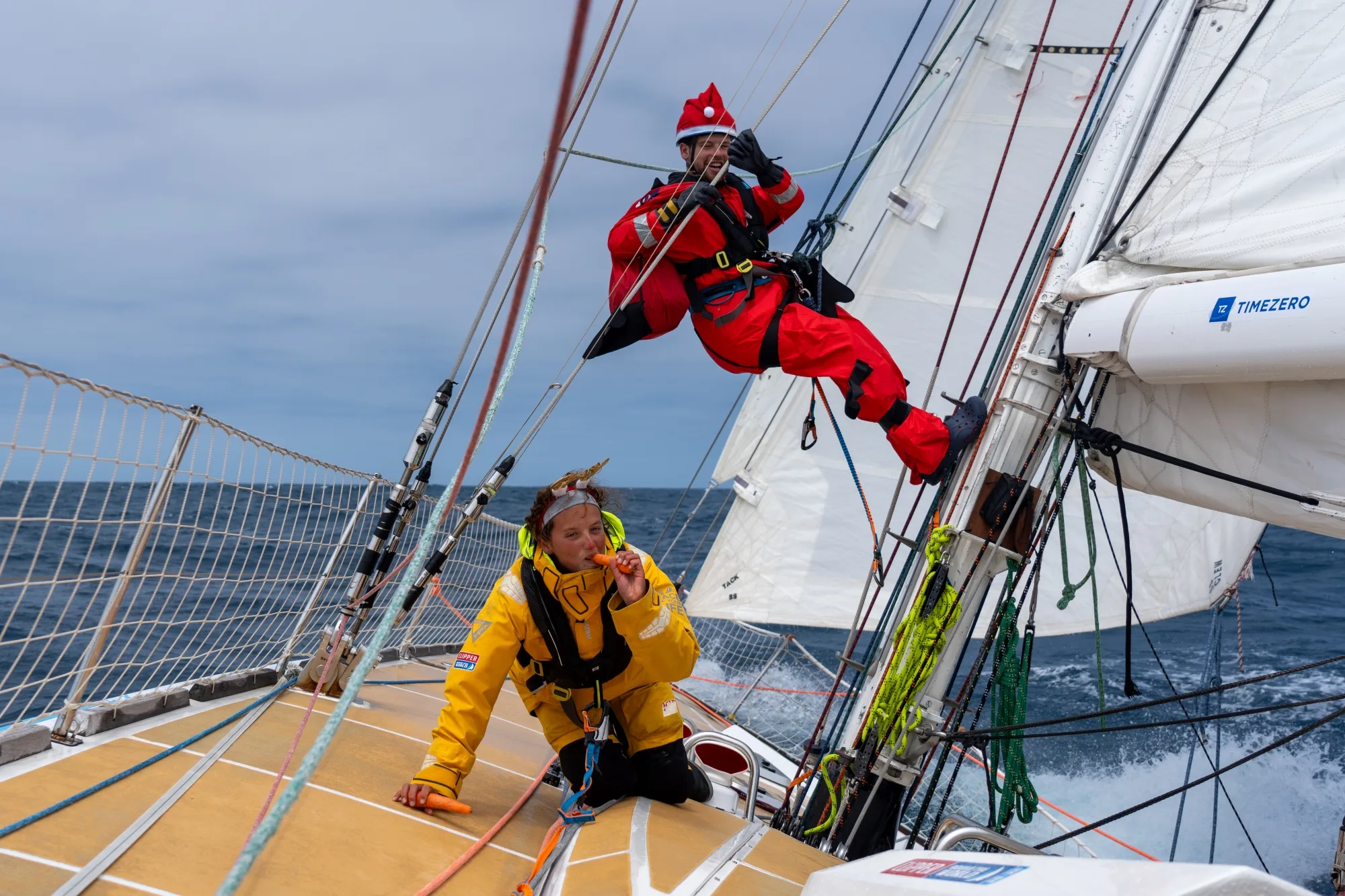 Great Ormond Street Hospital (GOSH) Clipper Race crew members on deck, with one sailor dressed as Father Christmas suspended from the rigging, the other dressed as Rudolf the red nosed reindeer, during an offshore ocean race.