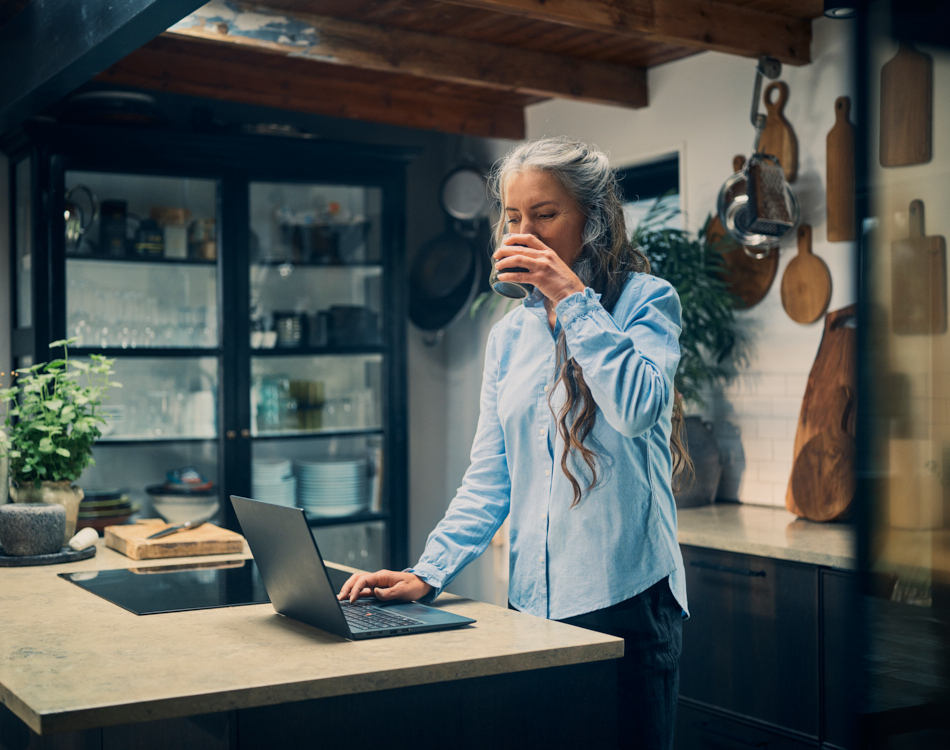 Kvinde drikker kaffe og arbejder hjemme ved sit bord