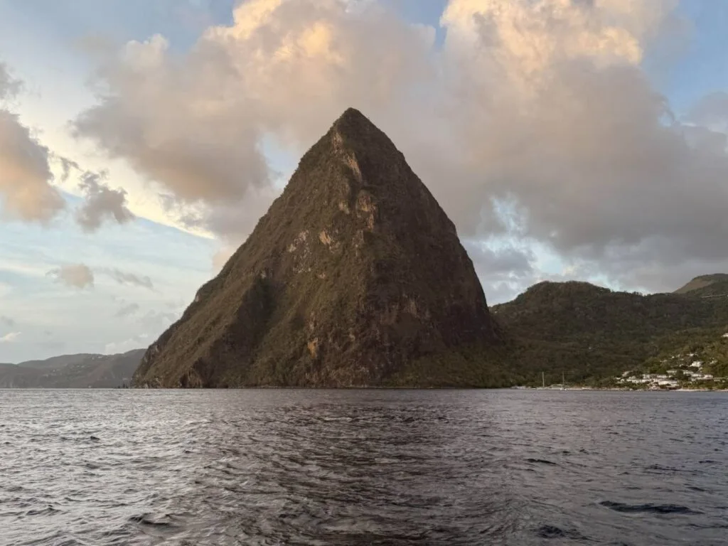 A steep, cone-shaped mountain peak rising from the sea, seen from the water under a partly cloudy sky