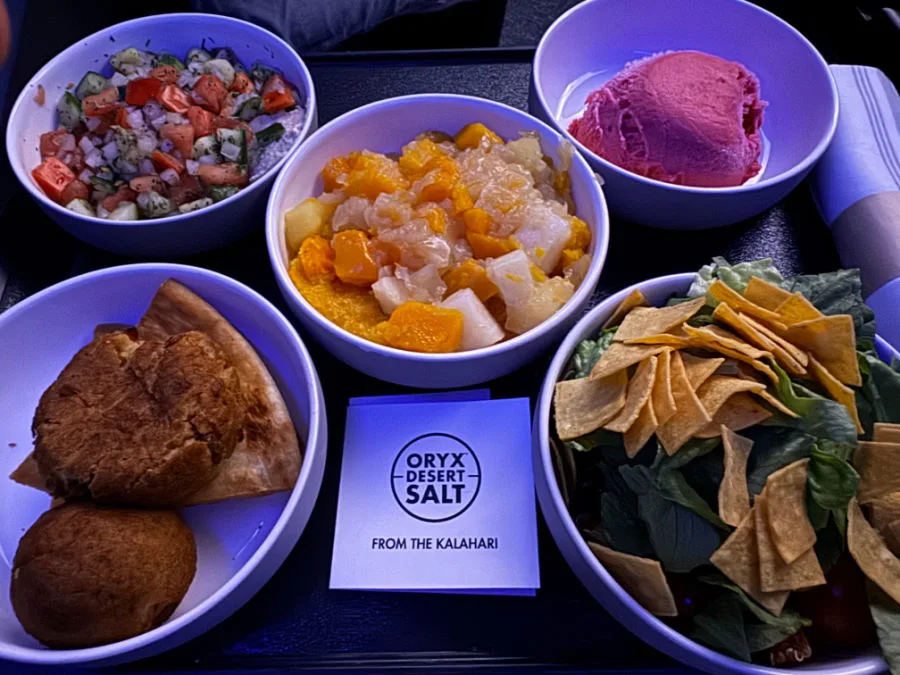 JetBlue Mint dinner service with side salads, bread rolls, a fruit dessert, and a leafy salad topped with tortilla strips