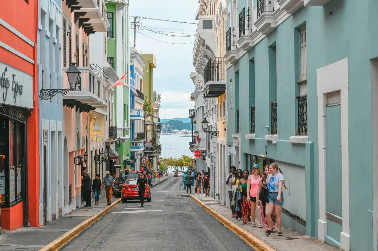 Colorful colonial buildings line a sloping cobblestone street in Old San Juan, Puerto Rico, with tourists walking toward the waterfront