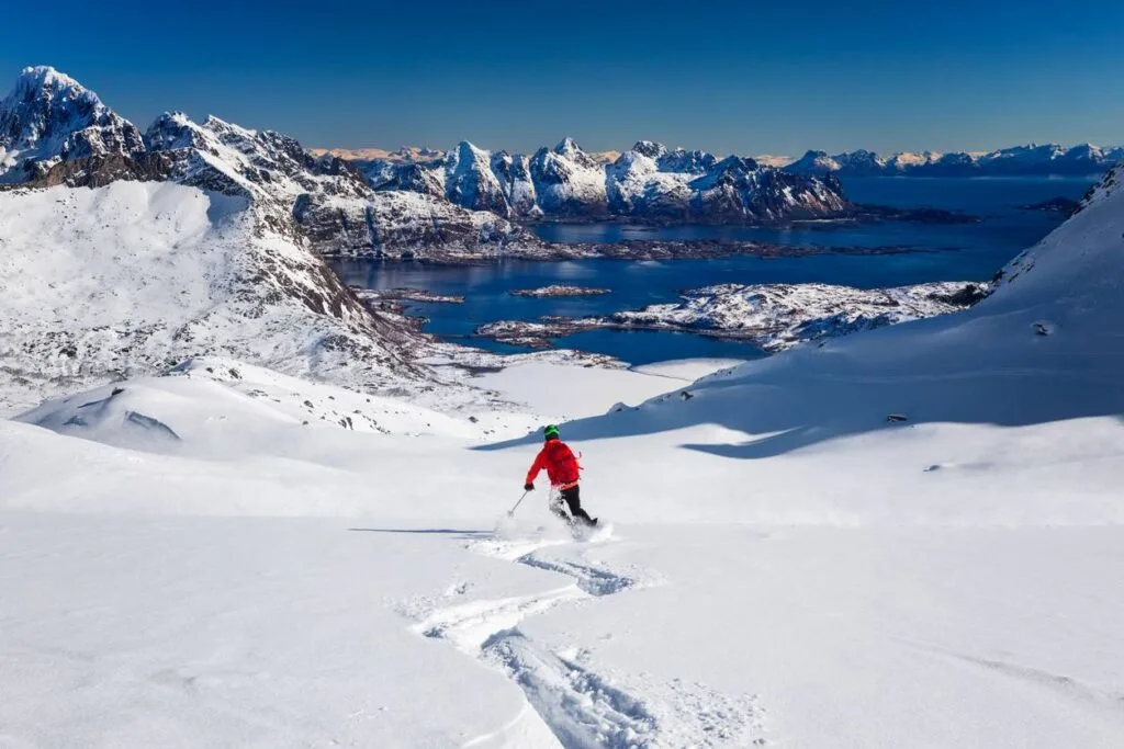 A skier carves fresh powder down a mountainside overlooking snow-covered fjords and islands in Norway