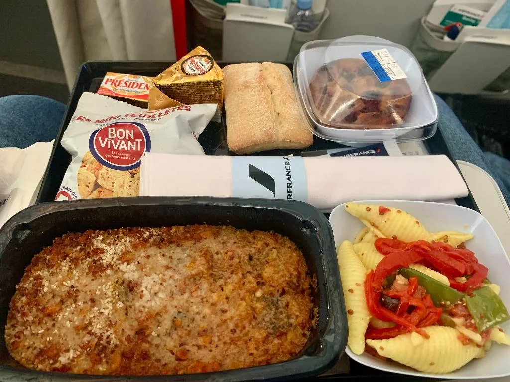 An Air France premium economy meal tray with pasta salad, a baked entree, cheese, bread, crackers, and a dessert